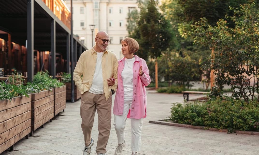 An older couple walking together along a tree-lined path.