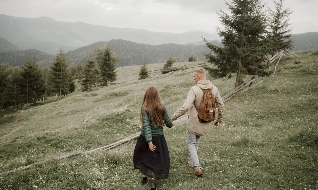 A couple walking through a grassy mountain meadow.