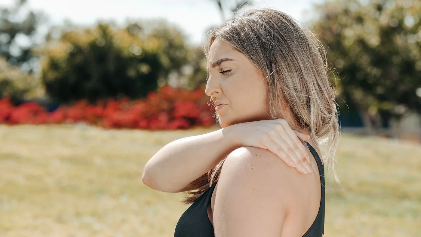 A woman resting her hand on her shoulder outdoors.