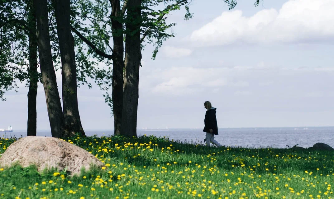 A woman walking through a sunlit lakeside meadow.