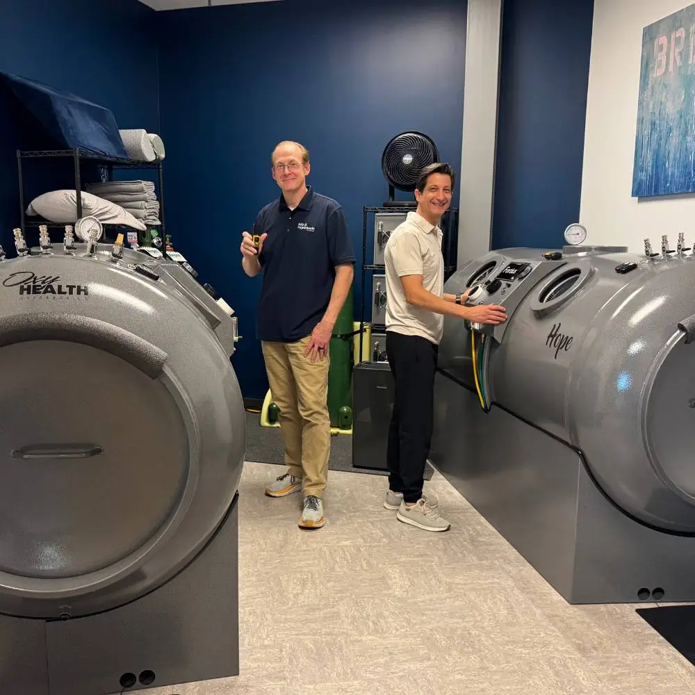 Two male technicians next to two hyperbaric chambers